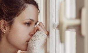 woman stand hand in face beside window feeling sad due to betrayal