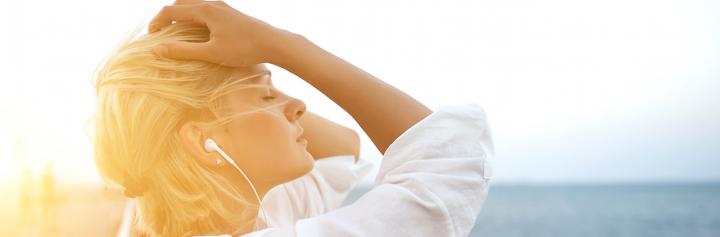 woman wearing earphones hands on hair eyes closed thinking in sunny sky
