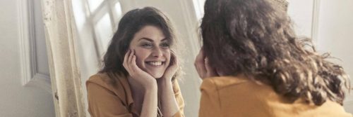 woman happily smiles looks herself in mirror