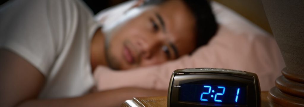 man lies on pink pillow tiredly looking at clock having insomnia problem