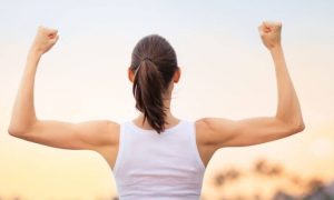 woman stands facing backward showing off muscles in sunset sky