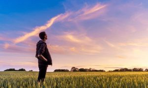 man stands alone in field hands in pocket looks at beautiful partially cloudy blue sky