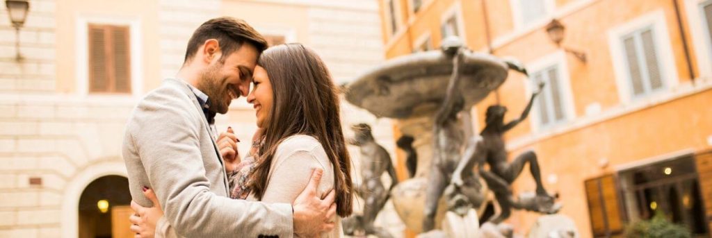 couple stands in front of building head to head hugging feeling loved smiling at each other