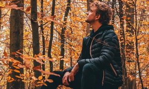 man sits on chair in red leaves forest feeling uncertain
