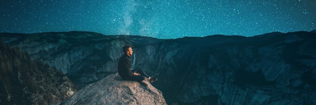 man sitting on on rock watching blue star sky