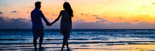 couple hand in hand happily walks along beach in sunset sky