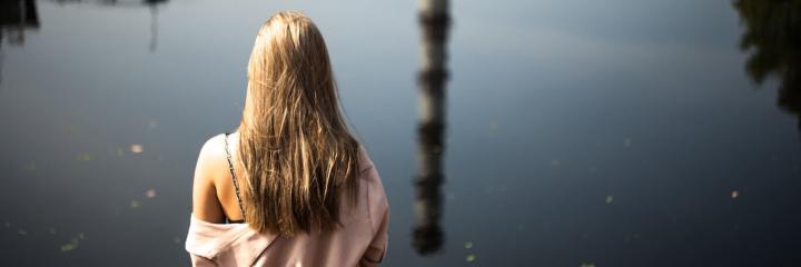 woman facing backward sits beside lake feeling isolated